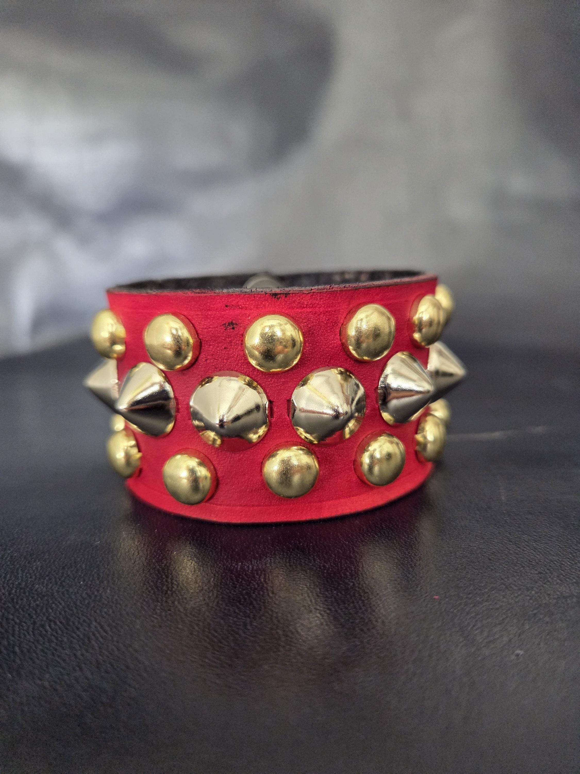 Red punk wrist cuff with silver and gold colored spikes.