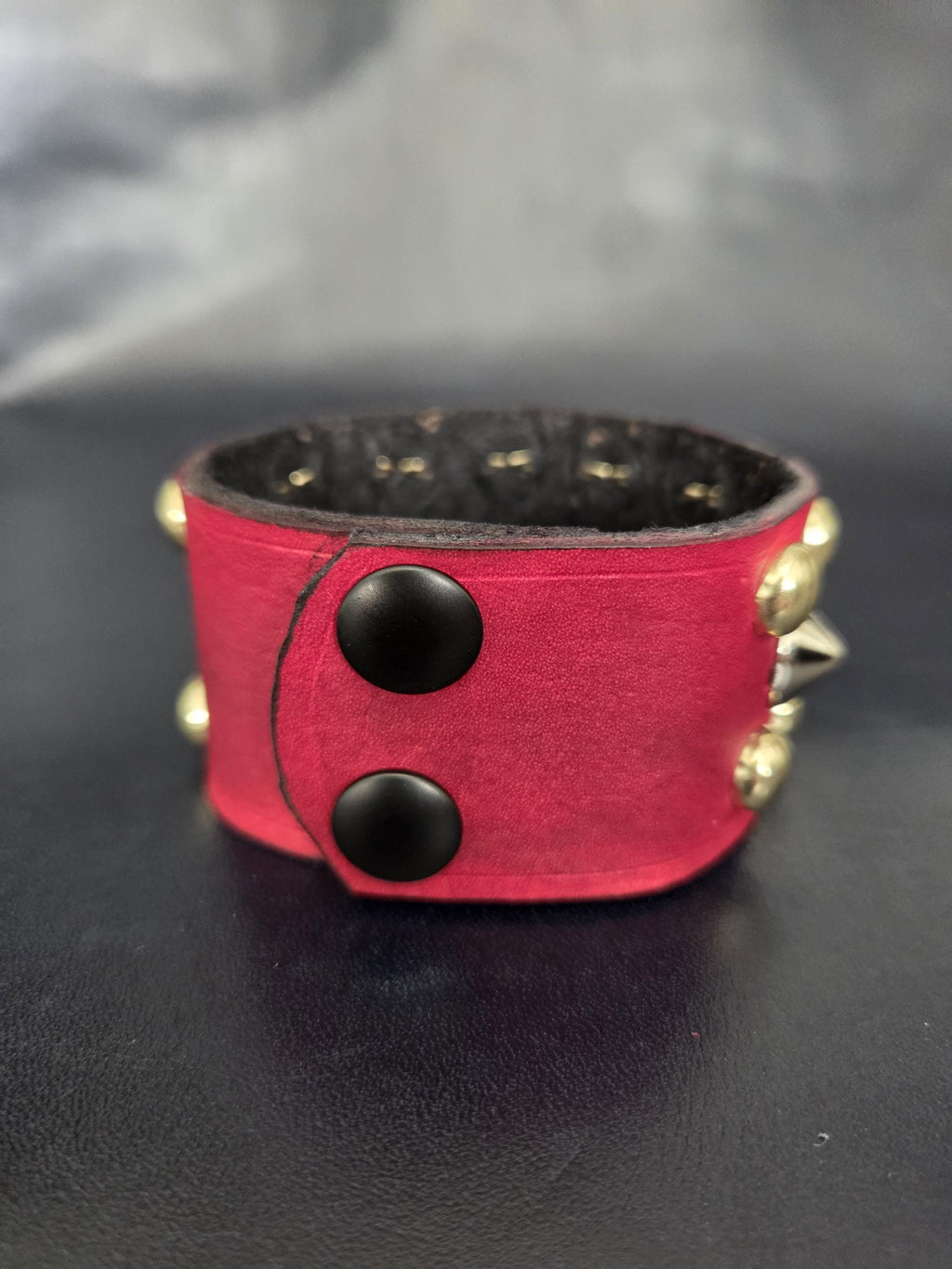 Red punk wrist cuff with silver and gold colored spikes.