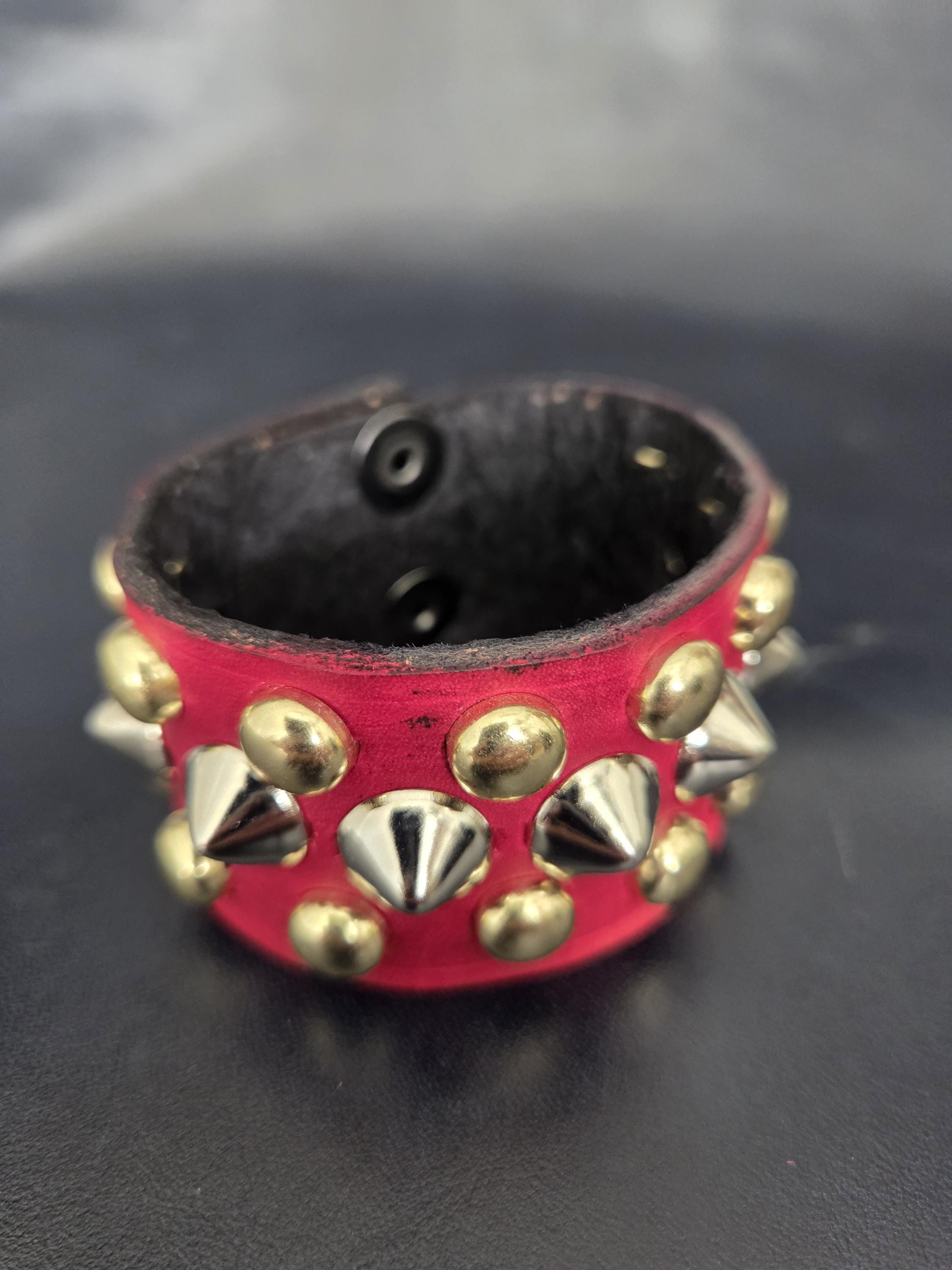 Red punk wrist cuff with silver and gold colored spikes.
